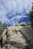 Large rock formation surrounded by pine trees under a partly cloudy blue sky