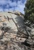 Large rocky formation with a small fire burning at its base surrounded by dry grass and trees under a partly cloudy sky