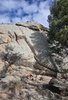 Large granite boulders with some sparse dry grass and pine tree branches, under a blue sky with scattered clouds