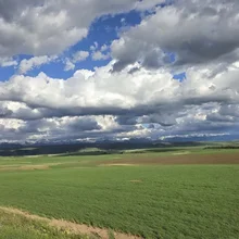 Wide green farmlands under a sky filled with large, dramatic clouds and distant mountain range