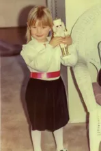 Smiling young girl wearing a white blouse with lace collar, black skirt, and red belt, holding a white and gold nutcracker doll