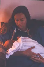 Person holding and looking down at a baby wrapped in a white blanket