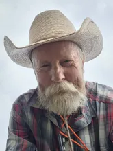 older man with a white beard wearing a large straw cowboy hat and a plaid shirt